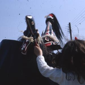 Children's Oss, child with club teasing Old Oss, against blue sky