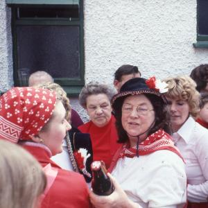 Old Oss women in red, holding beer bottle