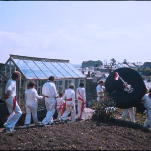 Old Oss, followed by procession, walking past greenhouse