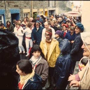 Old Oss dancing in rain, watched by spectators in raincoats