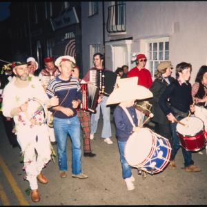 People in costume playing instruments walking along road at night