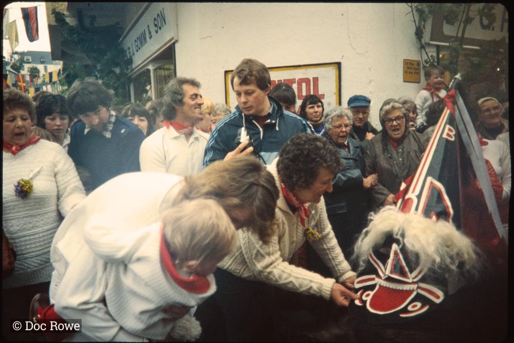 Old Oss hat being adjusted, woman holding baby to see 