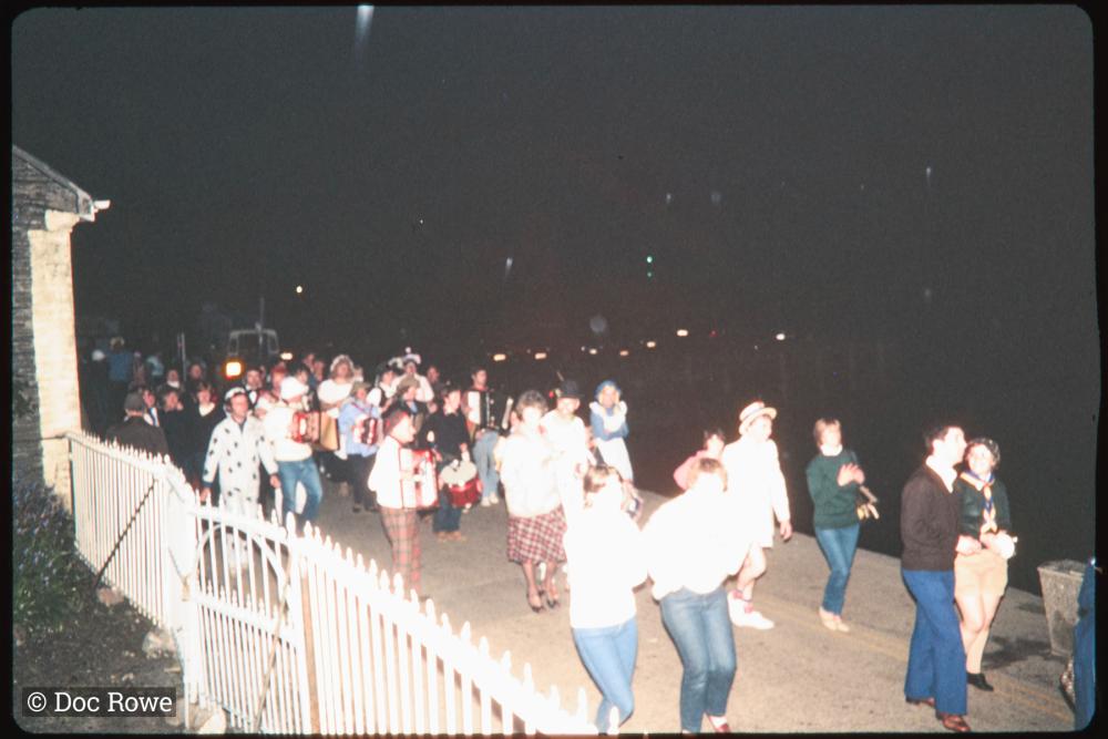 People in costume playing instruments walking along road at night