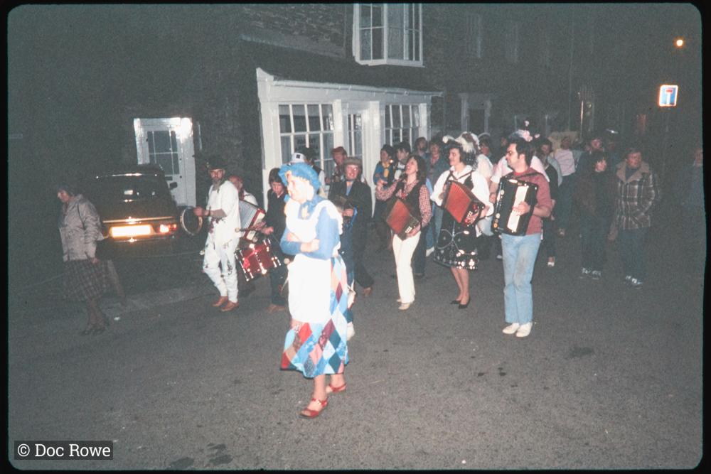 People in costume playing instruments walking along road at night