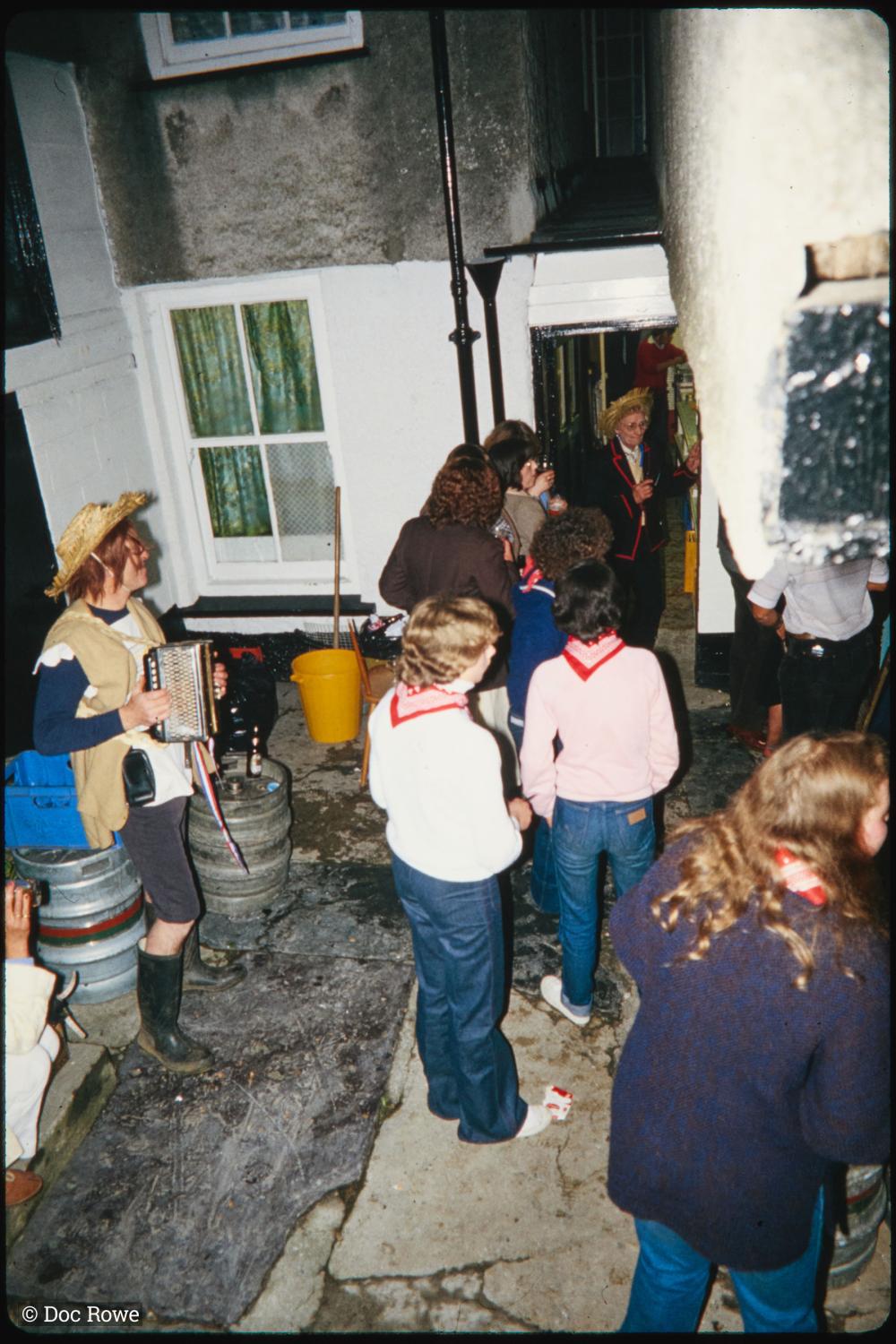 People stood in back yard of pub at night, accordion player playing