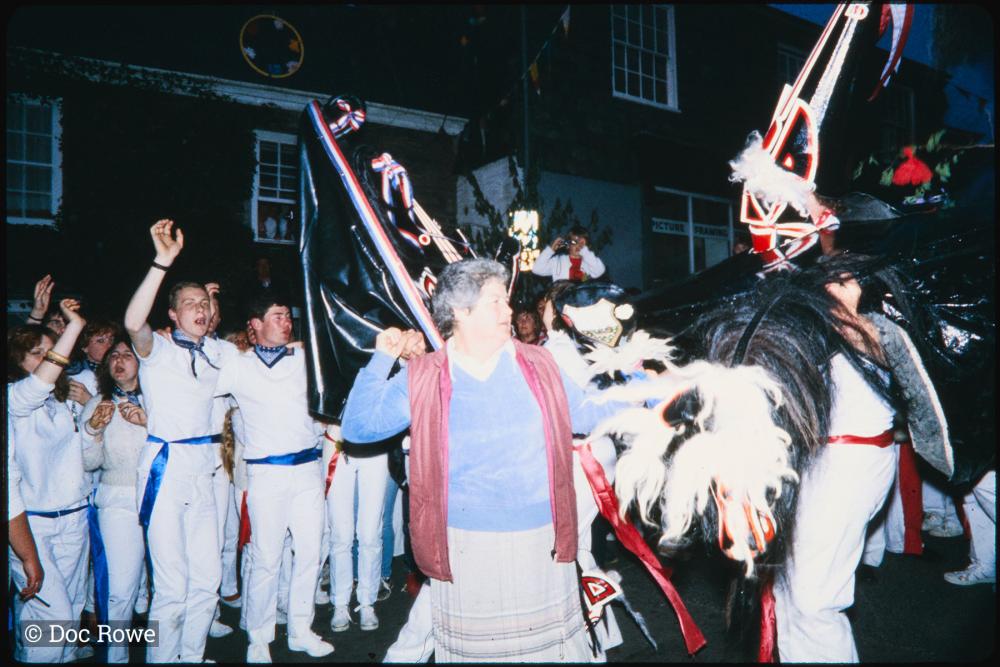 Woman dancing with Old Oss and Blue Ribbon under maypole at night