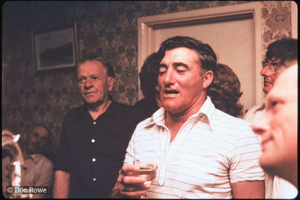 Man singing in pub, surrounded by people in fancy dress