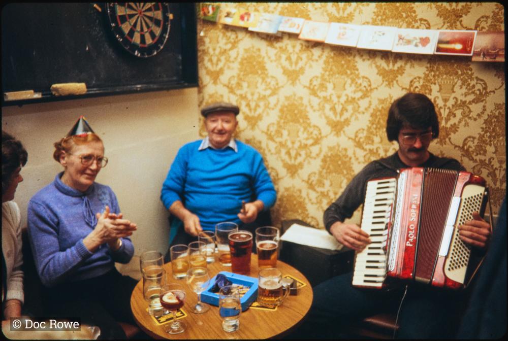 accordion player and people sat around table at pub 